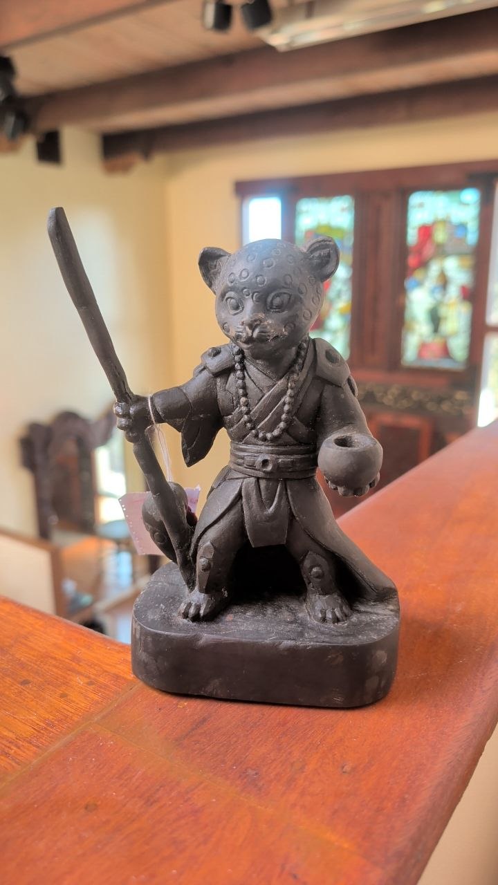 Hand-carved basalt stone statue of LeoChi on wooden table holding his protective walking staff and singing bowl