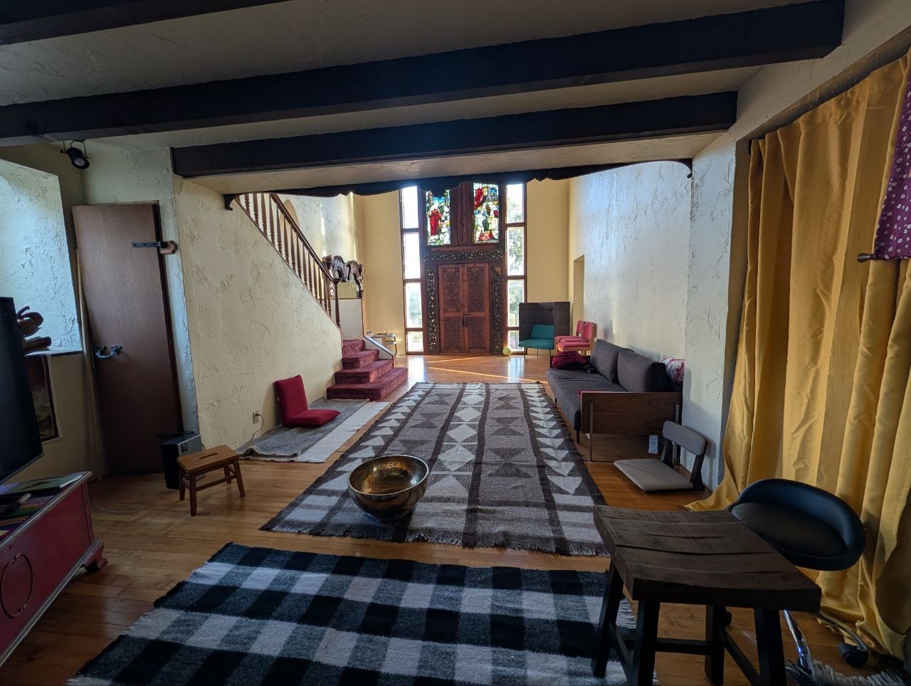 The Soaring Great Room at OmOrenda.space with double-height ceilings, stained glass, saffron curtains, and meditation runners